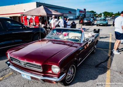 Burgundy convertible with its top down among vendor tents and parked cars in a plaza lot, Leica Q3