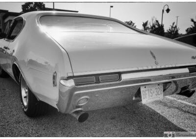 Monochrome rear quarter of the white hardtop, chrome bumper and exhaust tip on the asphalt, Leica Q3