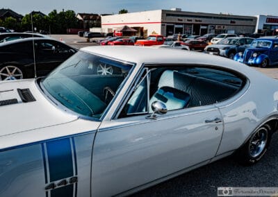The 442 badge on the blue stripe, chrome mirror and rows of show cars filling the lot behind, Leica Q3
