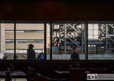 Looking out from a dark diner through a band of glass at steelwork and people passing, Leica Q2