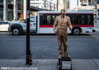 Up in the Six, a gold painted busker with a tip bucket beside a passing TTC bus downtown, Leica Q2