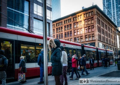 Crowd boarding a streetcar in the Six, an old brick building catching the last gold light, Leica Q2