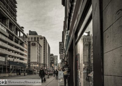 A wide grey avenue lined with construction, a man reading beside a shop window, Leica Q2