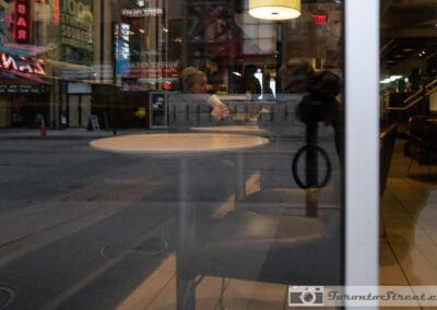 An empty round table behind storefront glass, the street and its neon laid over the frame, Leica Q2