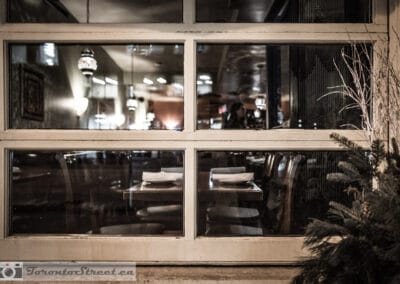 Empty set tables behind the white panes of a restaurant at night, every lamp still burning, Leica Q2