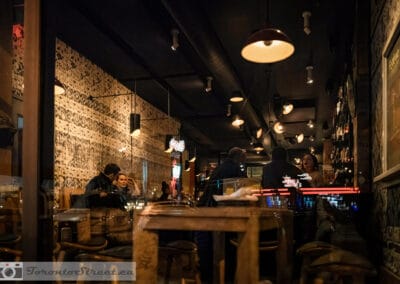 Patterned wallpaper and hanging lamps above a bar, people talking at the far end, Leica Q2