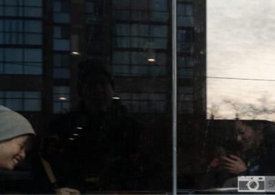 Young person laughing at a table at dusk, condo towers and sunset across the windows, Leica Q2