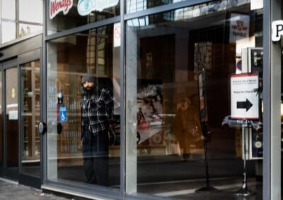 Man in a plaid shirt standing in a lobby behind glass, Loblaws and Dollarama signs above, Leica Q2