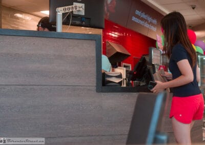 Young woman in running shorts waiting at the service counter, balloons and staff behind, Leica Q3