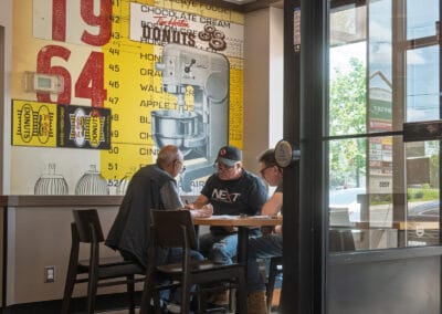 Three men working through paperwork inside Tim Hortons under a yellow 1964 donut price mural, Leica Q3