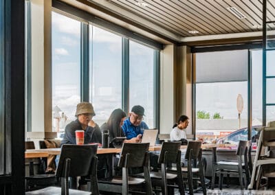 A row of people along a window counter, one on a laptop, empty chairs in the foreground, Leica Q3