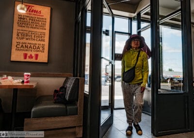 Woman in a wide sun hat stepping inside Tim Hortons past the Canada's Favourite Coffee sign, Leica Q3