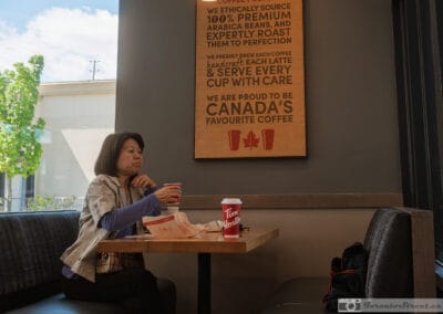 Woman alone in a booth with a Tim Hortons cup below the Canada's Favourite Coffee panel, Leica Q3