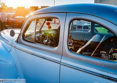 Side glass of the two-tone coupe with Frankenmuth AutoFest and NSRA stickers, plaza reflected, low sun flaring, Leica Q3