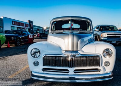 Head-on chrome grille and round headlights of the 1948 Mercury restomod, Canada flag lawn chair beside it, Leica Q3