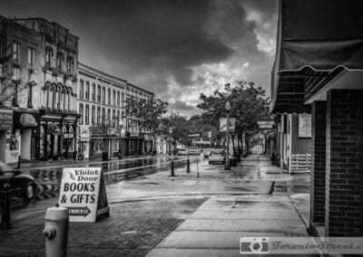 Black and white GTA street in the rain, a books and gifts sign on the wet brick sidewalk, Bowmanville, Fuji X-E2