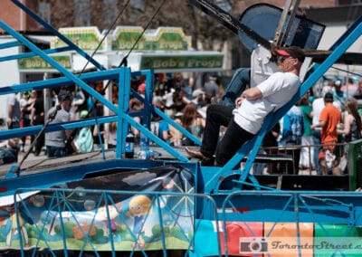 Ride operator resting in the blue steel of his own machine above a fairground crowd, Fuji X-E2