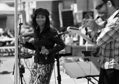Singer holding a microphone under a white tent while a musician plays beside her, Fuji X-E2