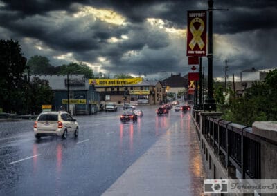 Rain falling on a suburban GTA road, Support Our Troops banners and tail lights under a storm sky, Fuji X-E2
