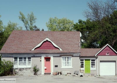 Grey brick house with a coral front door and a lime green side door, bright May afternoon, Leica Q3