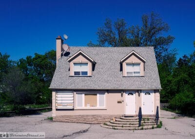 Pink stucco house with twin dormers and two white doors on an empty cracked lot, Leica Q3