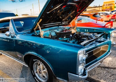 Hood up on a turquoise Pontiac convertible beside an orange coupe, plaza signs behind, north of Toronto, Leica Q3