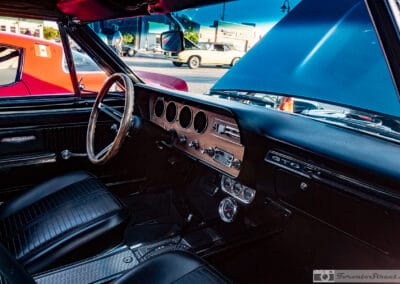 Wood rim wheel and four round dials on a turquoise Pontiac convertible dash, coffee sign across the lot, Leica Q3