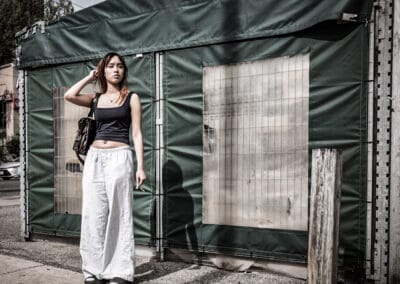 Young woman in a black top and wide white trousers against a green canvas hoarding on a Toronto street, Leica Q3