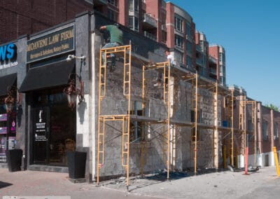 Two masons on yellow scaffolding stripping stone from a corner street front north of Toronto, Leica Q3
