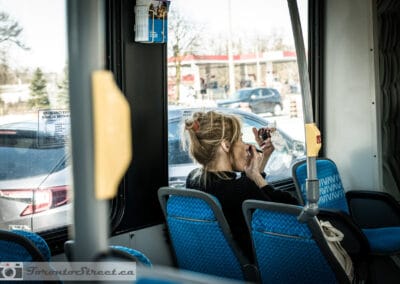 Woman doing her lipstick in a compact mirror on an almost empty VIVA bus, winter light outside, Leica Q2