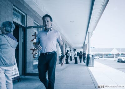 Man walking a suburban plaza sidewalk past a Chinese restaurant, students behind him, everyday scene, Leica Q3