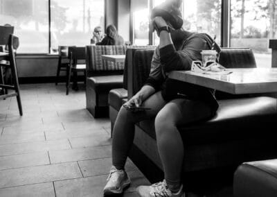 Woman in a coffee shop booth, headphones on, phone held low, a couple on their phones in the booth behind, Toronto, Leica Q3