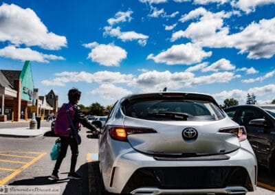 Shopper in a purple jacket reaching for a car door under a big cloud sky in a suburban lot, Leica Q3