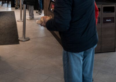 Man raising a hand to three young carollers in Christmas hats by the door of a coffee shop, Leica Q3