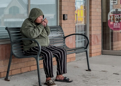 Woman in a green hoodie lighting up on a bench under a No Smoking sign, best camera is the one you have, taken on a phone