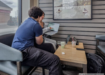 Young woman pointing at math on her laptop for a curly haired student, kayak picture on the wall, GTA, taken on a phone