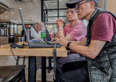 Two men studying a laptop screen at a coffee shop table, one in a cap and black vest, Toronto, taken on a phone